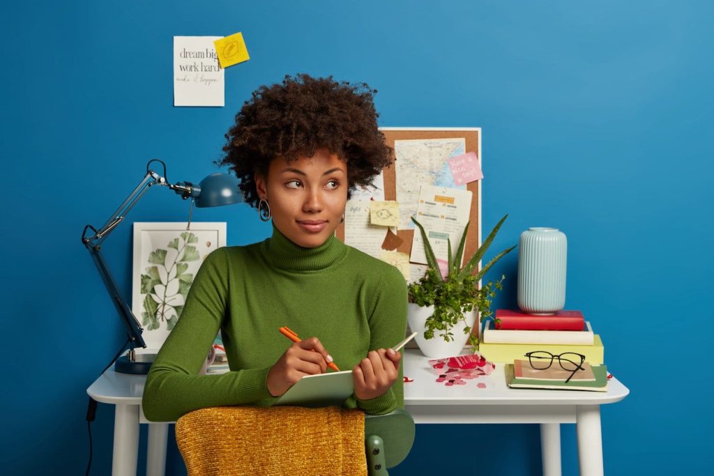 pensive curly young girl writes down future plans goals notepad thinks about good idea
